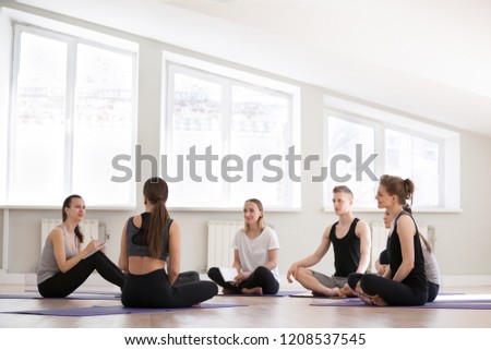 Group at yoga sport seminar in professional training studio. Girls and guys sitting together listen teacher coach ask questions communicating learn more about spiritual mental physical yoga practices Royalty-Free Stock Photo #1208537545