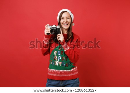 Stunning merry young Santa girl in knitted sweater, Christmas hat hold retro vintage photo camera isolated on red background. Happy New Year 2019 celebration holiday party concept. Mock up copy space