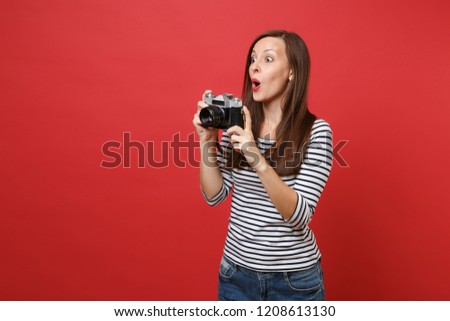 Amazed young woman holding retro vintage photo camera keeping mouth wide open, looking surprised isolated on bright red wall background. People sincere emotions, lifestyle concept. Mock up copy space