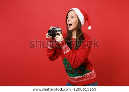 Surprised young Santa girl taking pictures on retro vintage photo camera, keeping mouth wide open isolated on red background. Happy New Year 2019 celebration holiday party concept. Mock up copy space