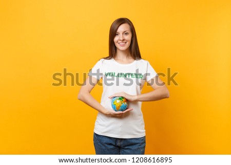 Portrait of woman in white t-shirt with written inscription green title volunteer hold in palms Earth world globe isolated on yellow background. Voluntary free assistance help, charity grace concept