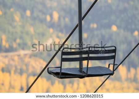 Fall colors on the hillside in the background of an empty ski chair.