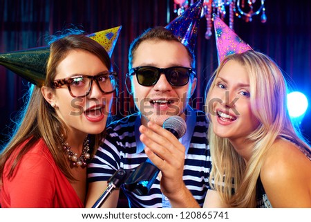 Portrait of happy friends singing in microphone in the karaoke bar