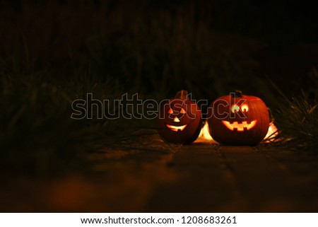 Scarved jack-o-lanterns are standing on the grass at night with lights. Happy Halloween Pumpkin. Night.