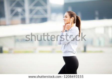 Pretty young sportswoman putting on headphones and listening to music in city.