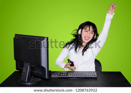 Happy business woman hears music with a mobile phone and headphone while dancing near her working table