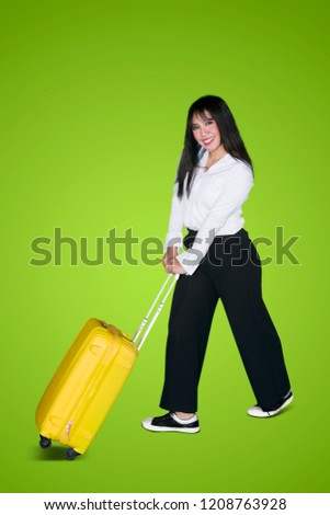 Portrait of a happy business woman carrying a luggage while walking in the studio with green screen