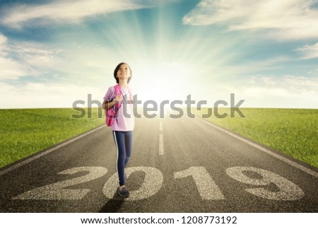 Picture of confident schoolgirl carrying a bag while standing above number 2019 on the highway with sunrise background