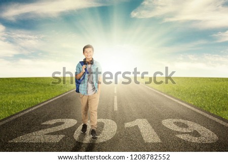 Picture of a happy preteen boy student walking above number 2019 on the road with sunrise background