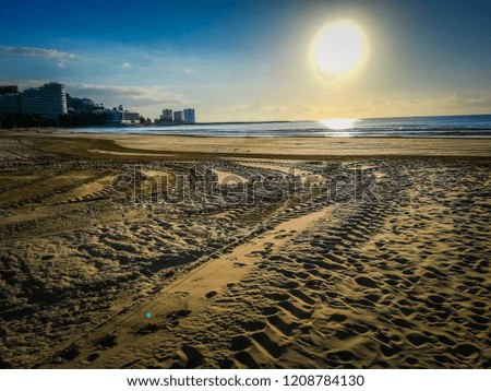 A photo of the beautiful Racó beach by the Mediterranean Sea the sunrise. The photo features the mountain and buildings of Cullera, which is a touristic seaside town in Valencia, Spain, Europe.