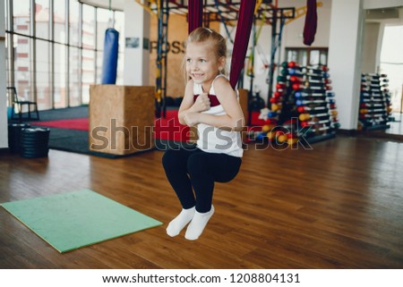 Little girl in a gym. Pretty little lady is engaged in flying yoga. Blonde on a white t-shirt and black leggings