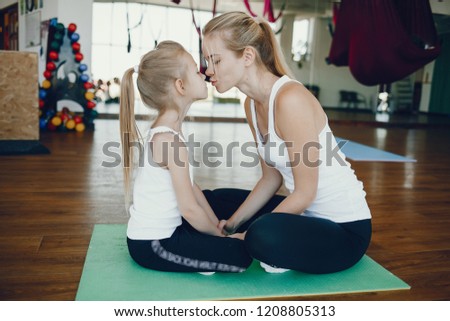 Mom and Daughter are doing yoga. Family in a gym. Little girl with mother in a white t-shirts and black leggings. Girls sitting on a green mat