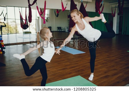 Mom and Daughter are doing yoga. Family in a gym. Little girl with mother in a white t-shirts and black leggings