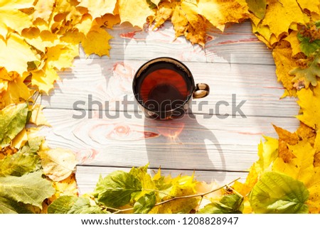 tea in a dark transparent cup with autumn leaves on a blue wooden table, in a cup a leaf of autumn