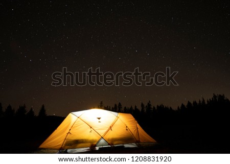 A tent lit up at night with trees and the stars above