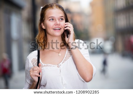 young positive female talking on phone at the modern street 
