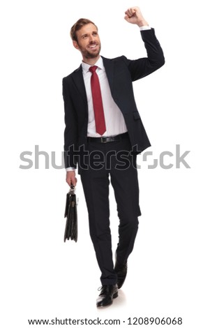 excited businessman walking forward on white background and celebrating while looking up to side and holding suitcase, full body picture
