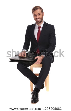 seated businessman waiting for job interview and opening suitcase while smiling, full body picture