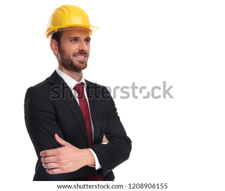 confident businessman wearing a yellow helmet looks up to side while standing on white background, portrait picture