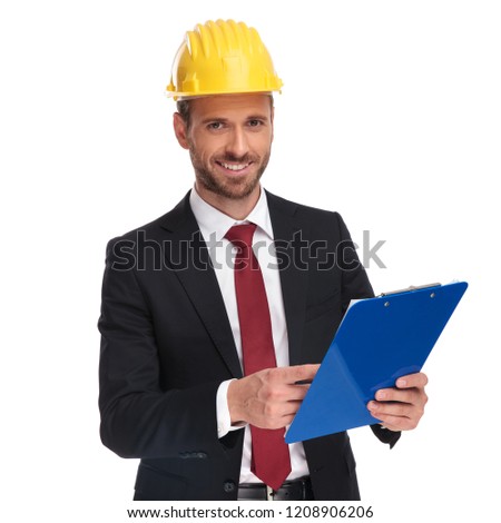 smiling businessman wearing a protection helmet holds blue files while standing on white background, portrait picture