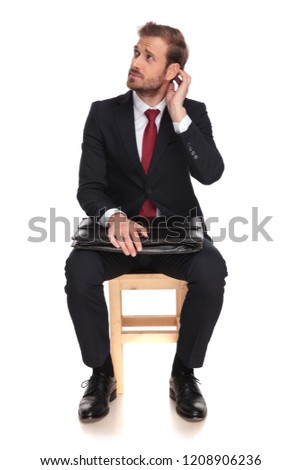 pensive businessman waits for interview and looks up to side while sitting on a wooden chair on white background and holding his head, full length picture