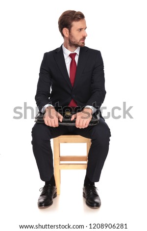serious businessman waiting for job interview looks to side while sitting on wooden chair on white background, full body picture