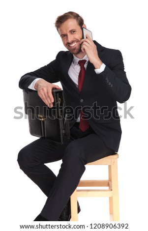 happy businessman sitting on wooden chair and waiting for interview while speaking on the phone, full length picture