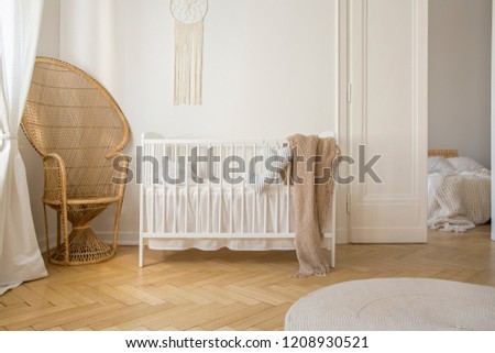 Wicker peacock chair next to white bedding in stylish kid bedroom, real photo