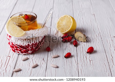 Treating cold. Cup with hot tea with lemon and berries stands on a table with tables and thermometer