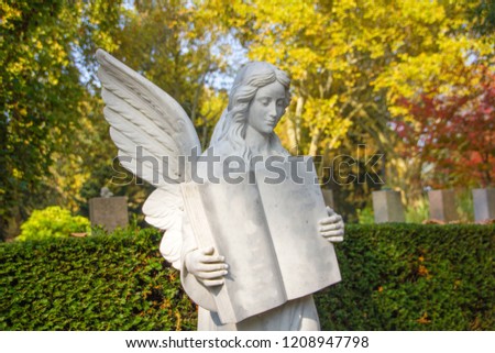 Angel figure made out of white stone during fall at a grave at a Christian cemetery. Symbol of sadness, grief, relief and rest in peace of loved family members.
