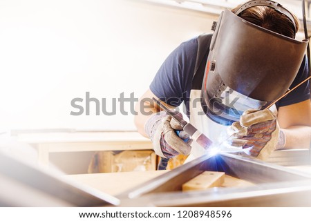 Male in face mask welds with argon-arc welding Royalty-Free Stock Photo #1208948596