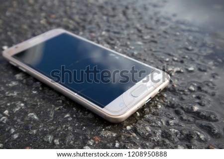 Modern smart phone with cracked screen glass lying in a puddle on the wet asphalt 