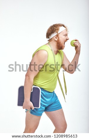 Funny picture of red haired, bearded, plump man on white background. Man holding an apple and scales
