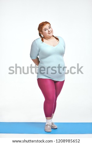 Funny picture of amusing, red haired, chubby woman on white background. Woman is shy