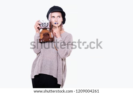 Portrait of young attractive woman in black cap, torn sweater, with blue lips, pink hair, holding retro camera in leather case, isolated on white background with copy-space