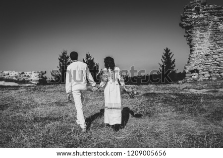 Newlyweds walk back on an rustic near the old stone wall in the autumn. Ukrainian style: woman, man in embroidered clothes on nature. Ethnic wedding in national costumes. Black and white photo.