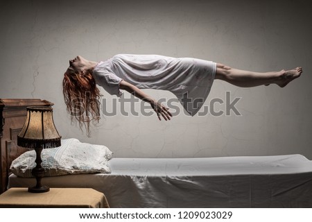 Woman levitating over bed / astral traveling, nightmare, excorcist halloween concept Royalty-Free Stock Photo #1209023029