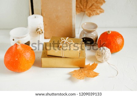 Still life on white background. Vintage books, wooden frame, dry maple leaves, golden gift boxes, red pumpkins, candles and decorations. Autumn concept