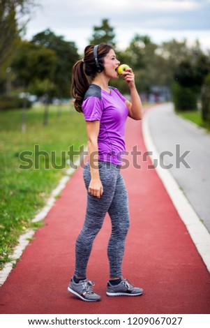Fitness woman listening music with headphones and eating green apple