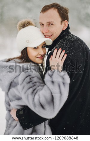 Stylish couple in love hugging in snowy mountains. Portraits of happy family gently embracing and smiling in winter mountains and forest. Holiday getaway together