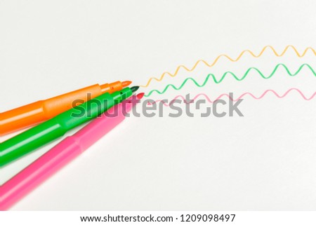 Three felt-tip pens of pink, orange and green color with drawn color marks on white background