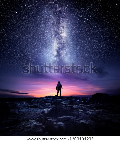 Night time long exposure landscape photography. A man standing in a high place looking up in wonder to the Milky Way galaxy, photo composite. Royalty-Free Stock Photo #1209101293