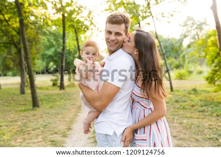 Joyful young family with little baby girl spending time together at the park, having a walk