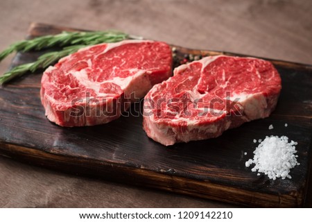 Two fresh raw rib-eye steak on wooden Board on wooden background with salt, pepper and rosmary in a rustic style Royalty-Free Stock Photo #1209142210