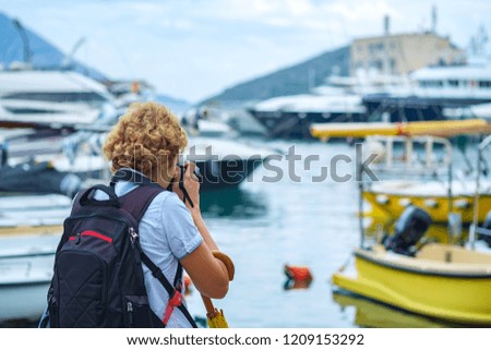 Photographer with a backpack taking travel photography. Woman photographer shooting with dslr camera walking along the promenade with beautiful maritime landscape in background.