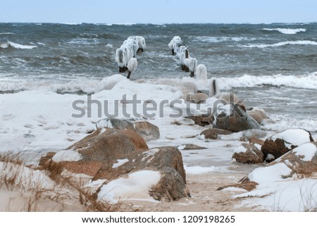 Old pier with snow and white ice in sea water waves in stormy weather blue sky winter windy day light