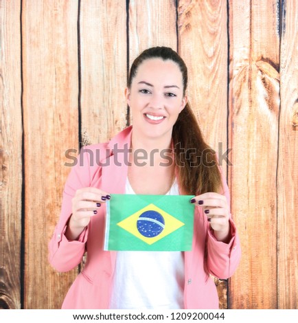 Beautiful young woman holding the flag of Brasil against a wooden background