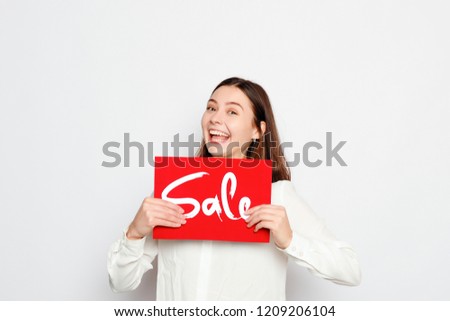 people, holidays, sale, shopping and advertisement concept - Young smiling brunette girl is holding a sale sign