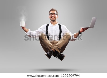 Young man is soaring in the air with a Cup of coffee and a laptop Royalty-Free Stock Photo #1209209794