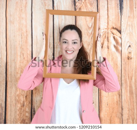 Happy young woman smiling while holding an empty picture frame against a wooden background